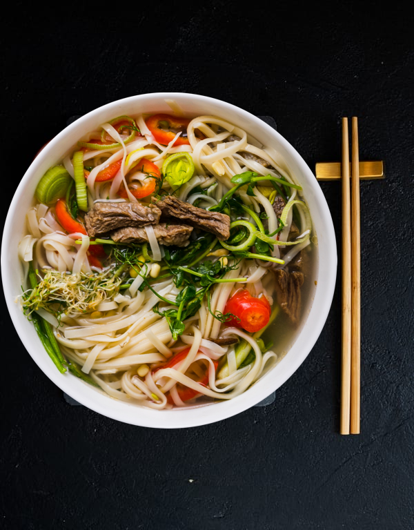 A large bowl of traditional Vietnamese pho with meat and vegetables.